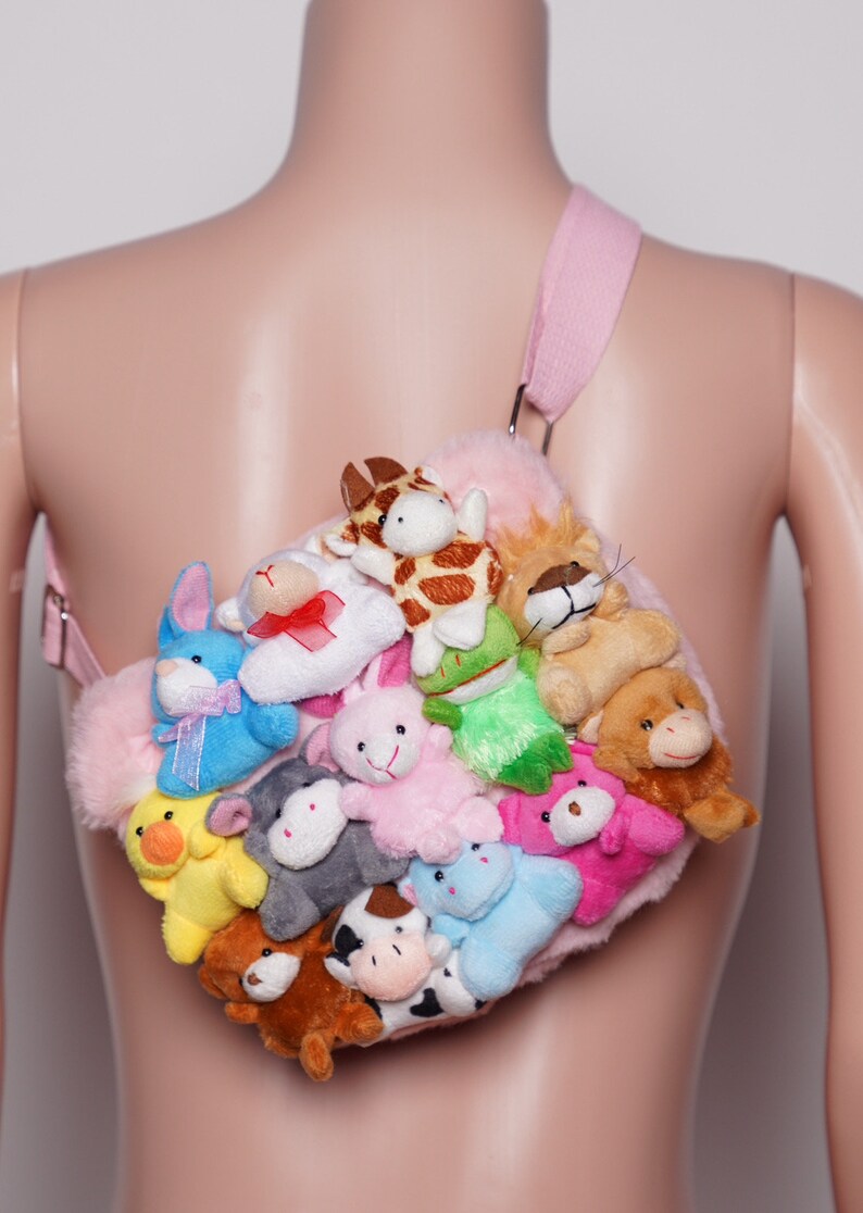 Pu&ograve; includere: Una borsa a tracolla in peluche rosa ornata da numerosi piccoli peluche. La borsa presenta una tracolla rosa chiaro e una variet&agrave; di peluche colorati, tra cui coniglietti, mucche e giraffe. La borsa &egrave; progettata per essere indossata a tracolla.