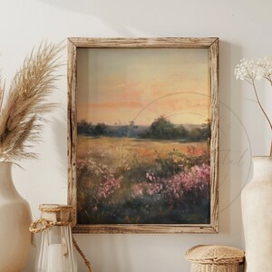 May include: A framed painting of a landscape with a field of wildflowers in the foreground and a forest in the background. The sky is a soft orange and pink color, and the sun is setting in the distance. The painting is hanging on a white wall, and there are two vases with dried flowers and a wicker basket on a wooden shelf below it.