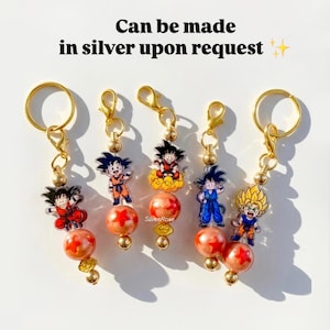 May include: Five keyrings with anime character designs. Each keyring has a gold-coloured ring and clasp, with a charm of a character and a large orange bead. The text "Can be made in silver upon request" is visible.