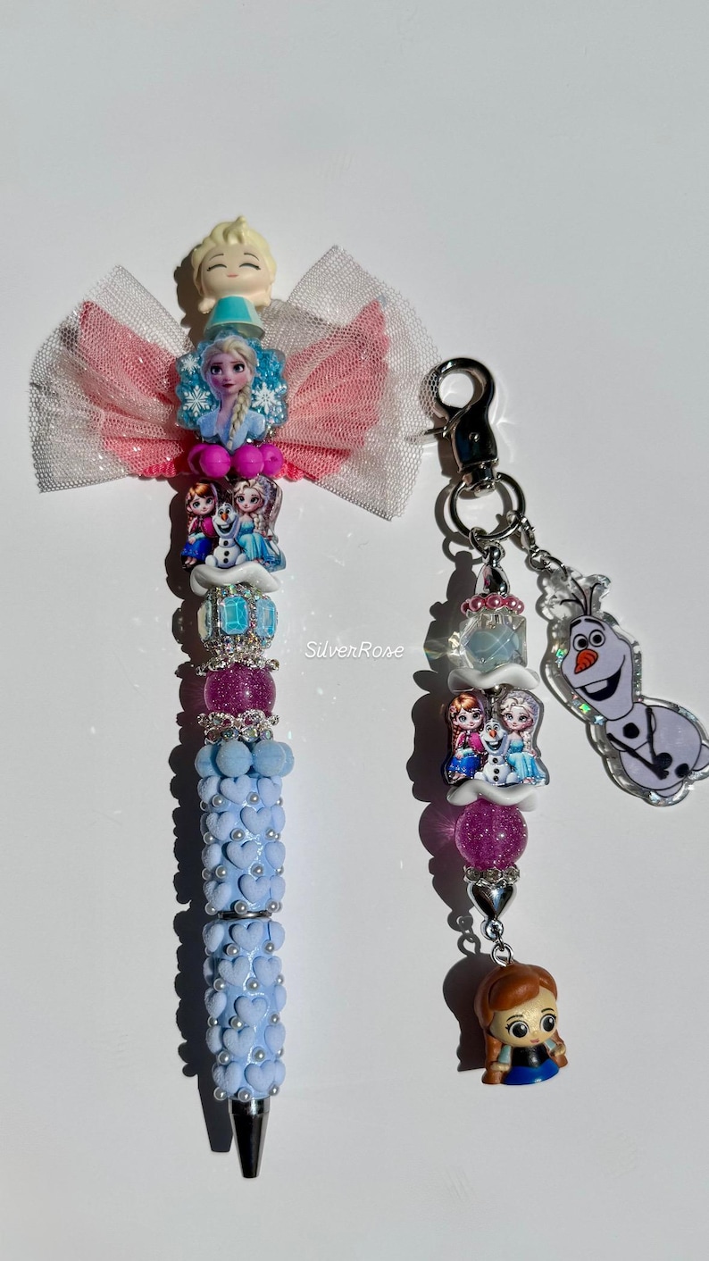 May include: A decorative pen and keychain set featuring characters from a popular animated film. The pen has a light blue barrel with heart-shaped accents and a bow. The keychain includes character charms and a silver clasp. The text "Silver Rose" is visible.