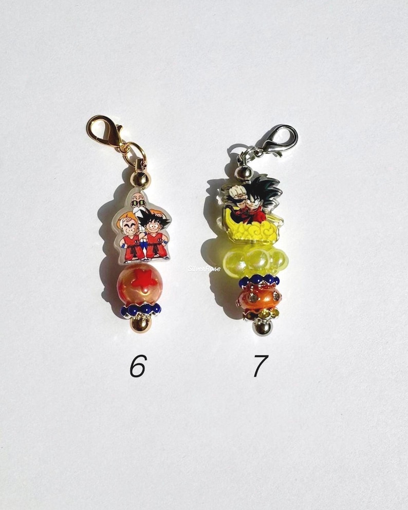 Puede incluir: Dos dijes decorativos etiquetados 6 y 7. El dije 6 tiene un broche de langosta dorado, una pieza acr&iacute;lica transparente con tres personajes, una cuenta naranja con una estrella roja y un acento azul. El 7 tiene un broche plateado, un personaje sobre una nube amarilla, una cuenta amarilla y una cuenta naranja con pedrer&iacute;a.