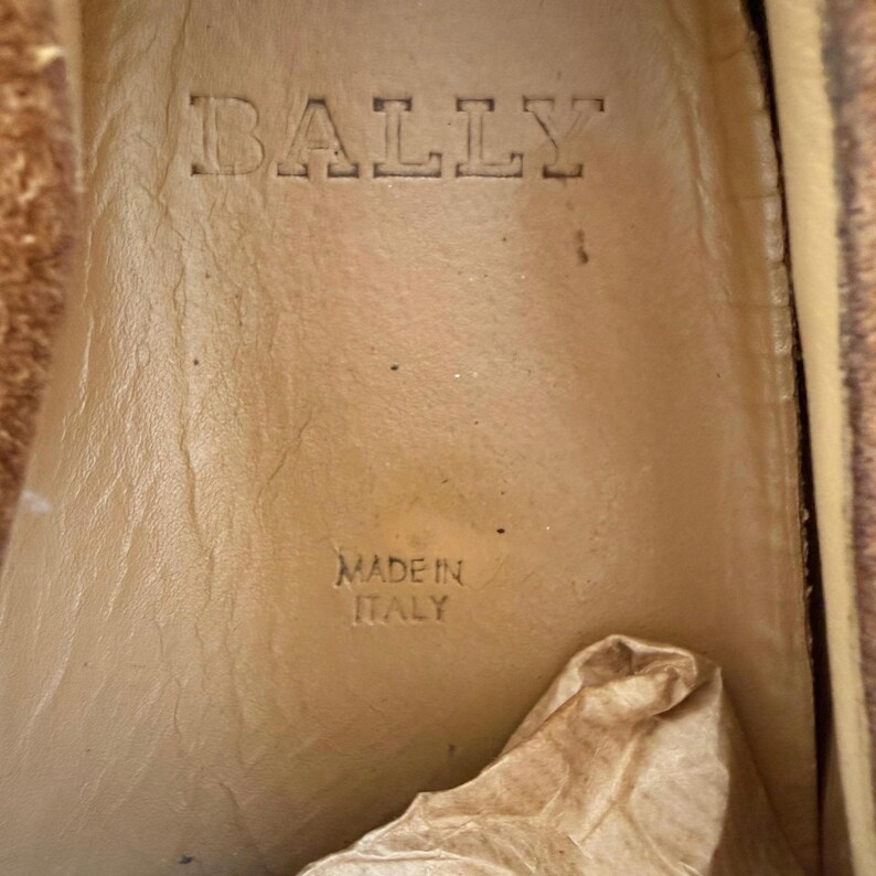 May include: Close-up of the interior of a shoe with the embossed brand name "BALLY" at the top. Below the brand name, the text "MADE IN ITALY" is stamped into the leather. The shoe's interior is a light tan color.
