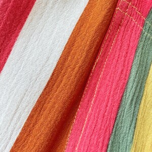 K&ouml;nnte beinhalten: Nahaufnahme eines farbenfrohen gestreiften Stoffes. Der Stoff weist kr&auml;ftige Streifen in Rot-, Orange-, Wei&szlig;-, Rosa-, Gr&uuml;n- und Gelbt&ouml;nen auf. Die Textur des Stoffes ist sichtbar, mit einem leicht geknitterten Aussehen. Die N&auml;hte sind mit gelben N&auml;hten sichtbar.