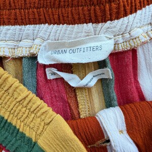K&ouml;nnte beinhalten: Nahaufnahme einer bunt gestreiften Shorts mit elastischem Bund. Die Shorts haben vertikale Streifen in Rot-, Orange-, Gelb-, Gr&uuml;n- und Wei&szlig;t&ouml;nen. Das Etikett lautet "Urban Outfitters".