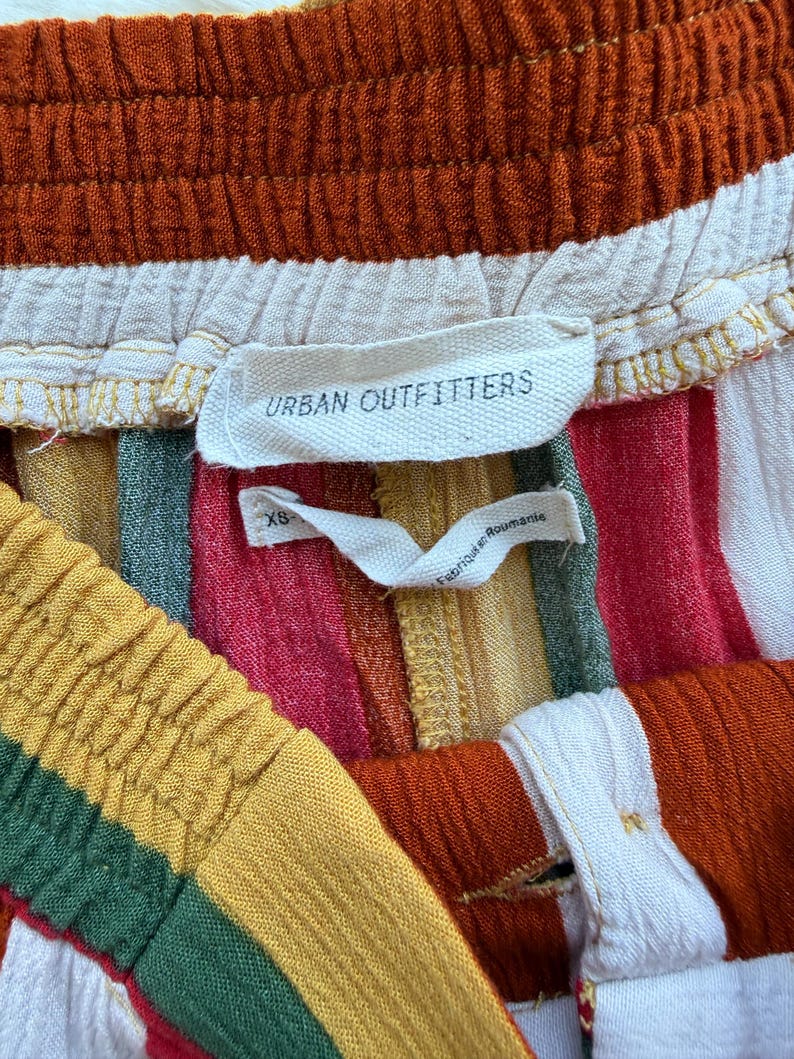 K&ouml;nnte beinhalten: Nahaufnahme einer bunt gestreiften Shorts mit elastischem Bund. Die Shorts haben vertikale Streifen in Rot-, Orange-, Gelb-, Gr&uuml;n- und Wei&szlig;t&ouml;nen. Das Etikett lautet "Urban Outfitters".