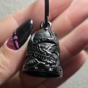 Può includere: Campanella da moto nera con un disegno di aquila e la scritta "LIVE TO RIDE, RIDE TO LIVE". La campanella è sospesa a un anello di metallo nero.