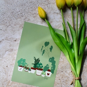 Peut inclure: Une carte verte avec une illustration botanique de plantes en pot, accompagnée d'un bouquet de tulipes jaunes attachées avec de la ficelle. La carte présente diverses espèces de plantes dans des pots blancs à bords rouges, et un détail en forme de cœur.