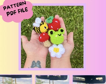 May include: Crochet car charms featuring a bee, frog, strawberry, mushroom, and flower. The charms are hanging from the rearview mirror of a car. The image also shows a close-up of the charms in a person's hand. The text "LSCRAFTSANDCROCHET" and "PATTERN PDF FILE" is visible in the image.