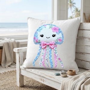 May include: White square pillow featuring a whimsical jellyfish design. The jellyfish has a light blue head with pink floral accents and a smiling face. Pink polka dot bow and blue and pink striped tentacles complete the design. The pillow is on a white bench.
