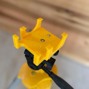 Może przedstawiać: Żółty uchwyt Topcon DeWalt przymocowany do żółtego i szarego statywu. Uchwyt ma nadrukowane logo DeWalt i numer modelu. Statyw ma regulowane nogi i czarny uchwyt.