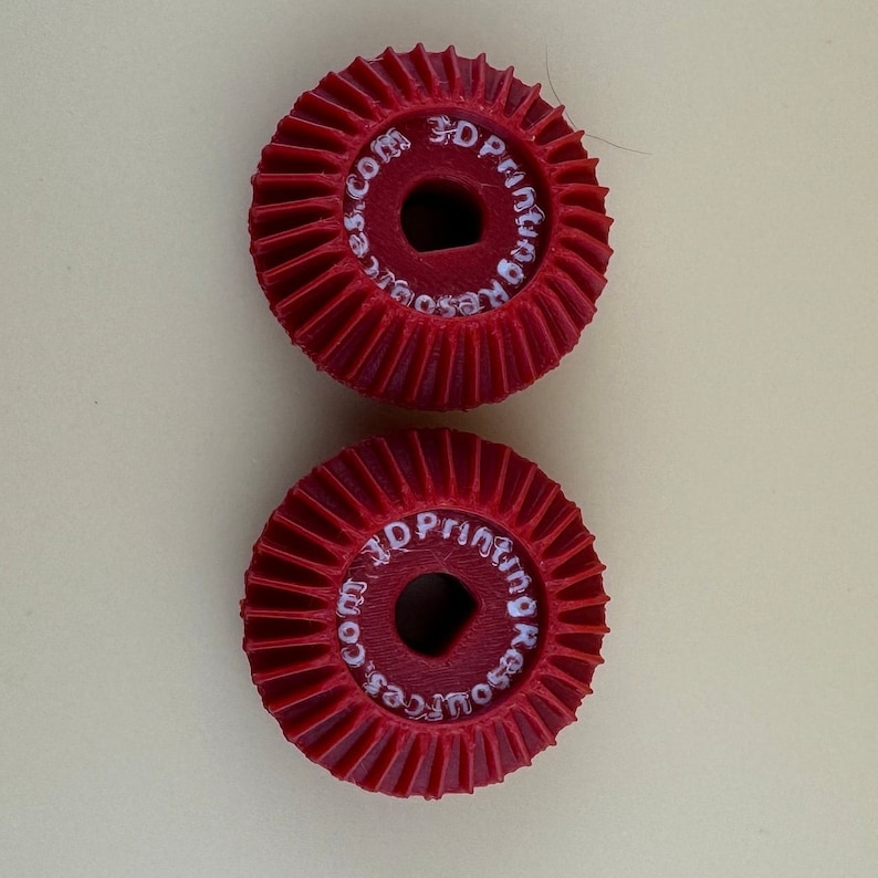 Puede incluir: Dos engranajes de pl&aacute;stico rojo con una inscripci&oacute;n blanca que dice "3D Printing Resources.com".