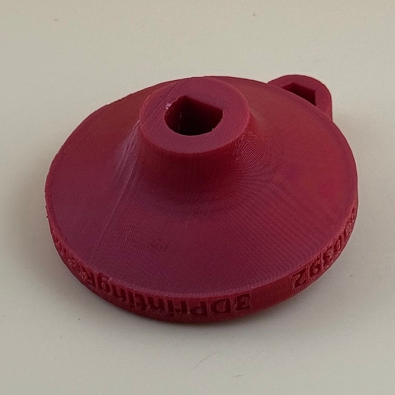 May include: A red plastic 3D printed object with a square hole in the centre and the text "3D Printing" around the edge.