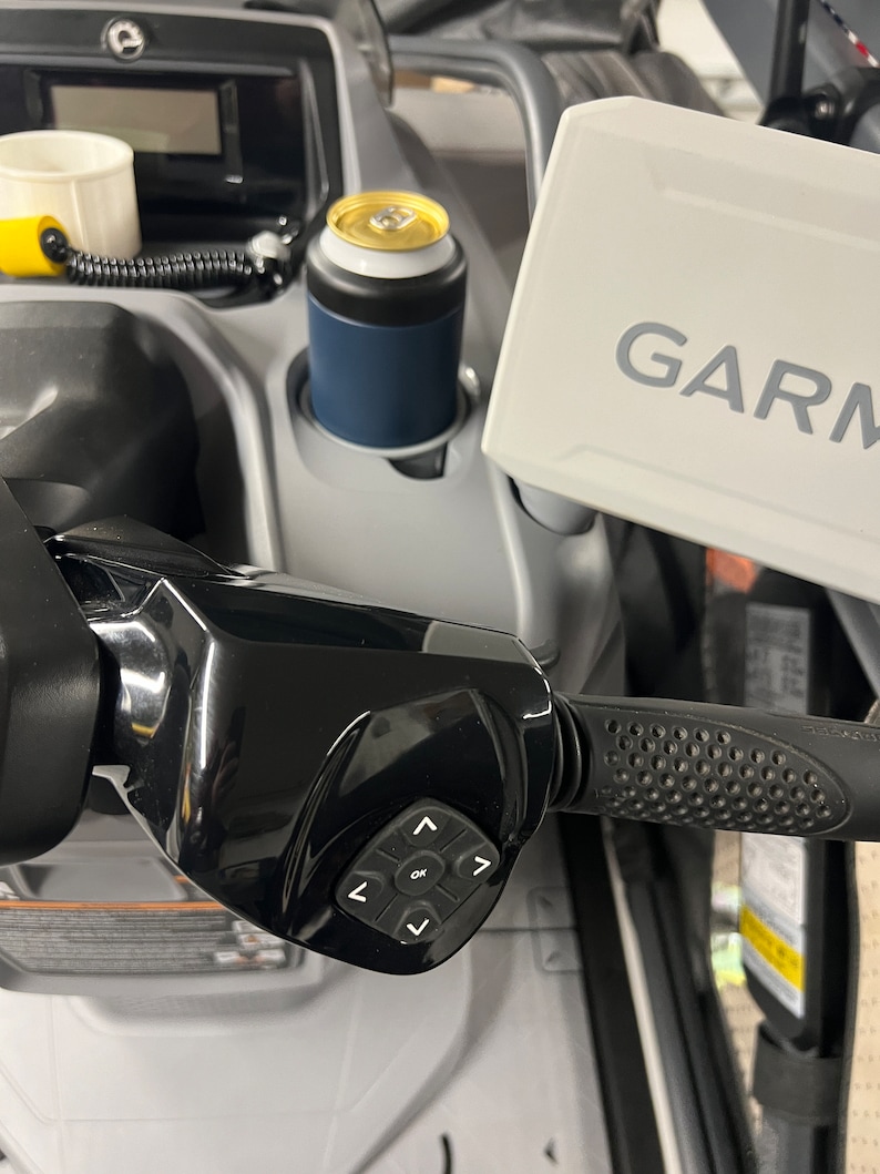 Puede incluir: Primer plano del manillar de una moto de nieve con un panel de control negro y un dispositivo Garmin. Un enfriador de latas azul y blanco contiene una bebida. El manillar tiene un agarre texturizado.