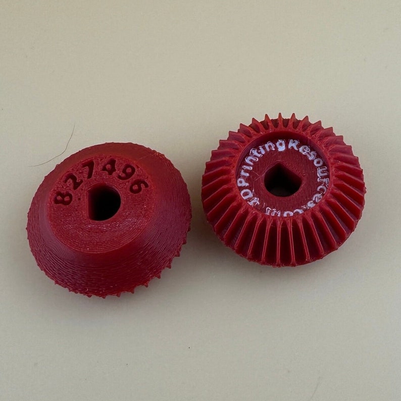 Puede incluir: Dos engranajes de pl&aacute;stico rojo, uno con el n&uacute;mero "827496" impreso en &eacute;l y el otro con el texto "Resoluci&oacute;n de impresi&oacute;n 3D" impreso en &eacute;l.