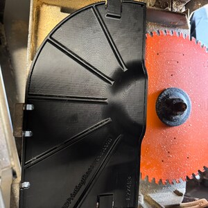Pu&ograve; includere: Un parascintille per lama da sega in plastica nera con il testo "3DPrintingResource.com" e "827458" stampato su di esso. Il parascintille &egrave; fissato a una lama da sega con una lama rossa e argentata.