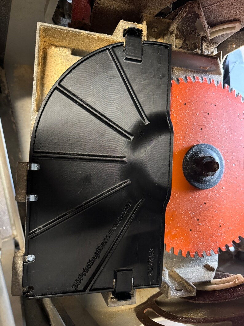 Pu&ograve; includere: Un parascintille per lama da sega in plastica nera con il testo "3DPrintingResource.com" e "827458" stampato su di esso. Il parascintille &egrave; fissato a una lama da sega con una lama rossa e argentata.