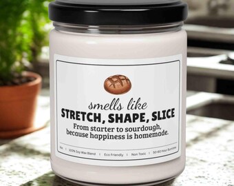 May include: A white candle in a glass jar with a black lid. The label reads "smells like STRETCH, SHAPE, SLICE" with a bread illustration. Text below says "From starter to sourdough, because happiness is homemade."
