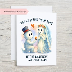 May include: A white greeting card with a watercolor illustration of two ghost figures. One ghost is kneeling and offering a pumpkin ring to the other. Text reads "YOU'VE FOUND YOUR BOO!" and "LET THE HAUNTINGLY EVER AFTER BEGIN!"