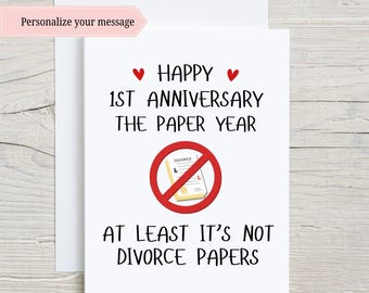 May include: A white card with a red heart, black text that reads "Happy 1st Anniversary The Paper Year" and a red circle with a diagonal line through it. Inside the circle is a yellow paper with the word "Divorce" written on it. Below the circle is black text that reads "At least it's not divorce papers."