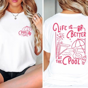 Peut inclure: T-shirt blanc avec un motif rose sur le devant qui dit "Pool Life" et un motif rose au dos qui dit "Life is Better at the Pool" avec un soleil, un plongeoir, un flamant rose gonflable et un cornet de glace.