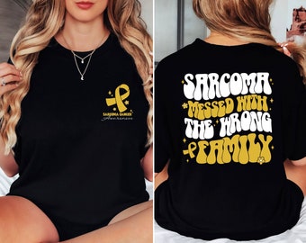 May include: Black t-shirt with a gold ribbon and the text "Sarcoma Cancer Awareness" on the front. The back of the shirt has the text "Sarcoma *Messed With* The *Wrong* Family" in a retro font with gold accents.