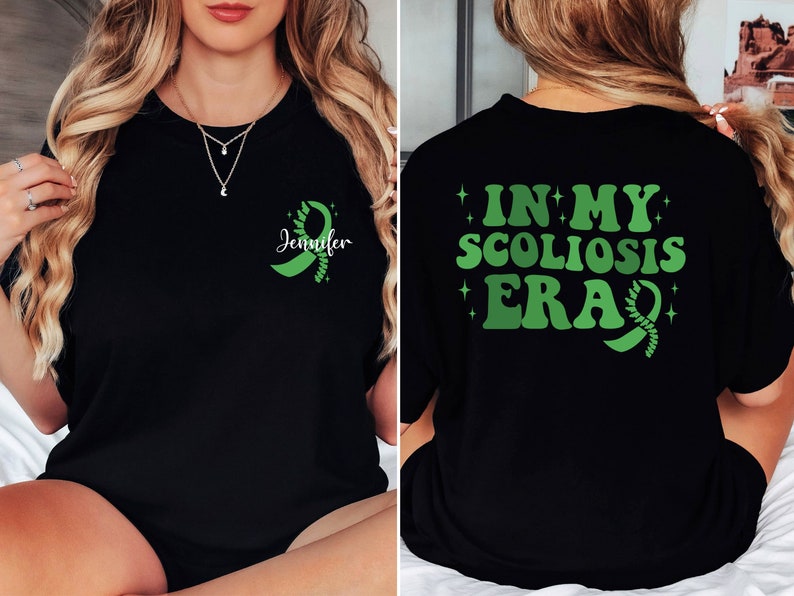 Pu&ograve; includere: Maglietta nera con un nastro verde e il testo "Jennifer" sul davanti. La parte posteriore della maglietta ha il testo "In My Scoliosis Era" con un nastro verde.