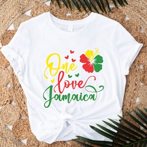 May include: White t-shirt with the text "One love Jamaica" in green, yellow, and red lettering. A red, yellow, and green hibiscus flower is above the text.