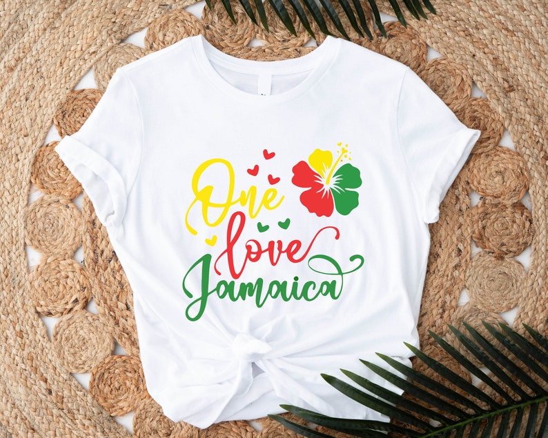 May include: White t-shirt with the text "One love Jamaica" in green, yellow, and red lettering. A red, yellow, and green hibiscus flower is above the text.