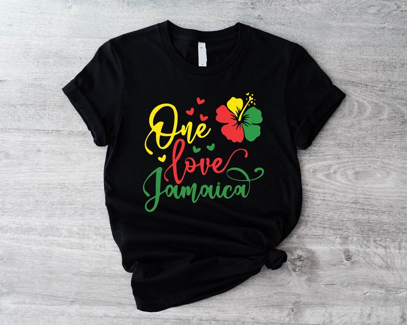 May include: Black t-shirt with the text "One love Jamaica" in yellow, green, and red lettering. A red, yellow, and green hibiscus flower is above the text.