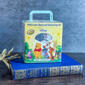 May include: A Disney "First Concepts" CD set featuring Winnie the Pooh and friends. The box has a light blue handle and includes a "Learn Aloud Book" and a CD. The box is yellow with character illustrations and text.
