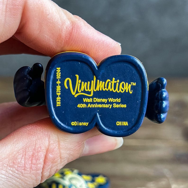 May include: A dark blue Vinylmation figure with the text "Vinylmation" in yellow script. The figure is from the Walt Disney World 40th Anniversary Series. The bottom of the figure reads "&copy;Disney" and "CHINA".