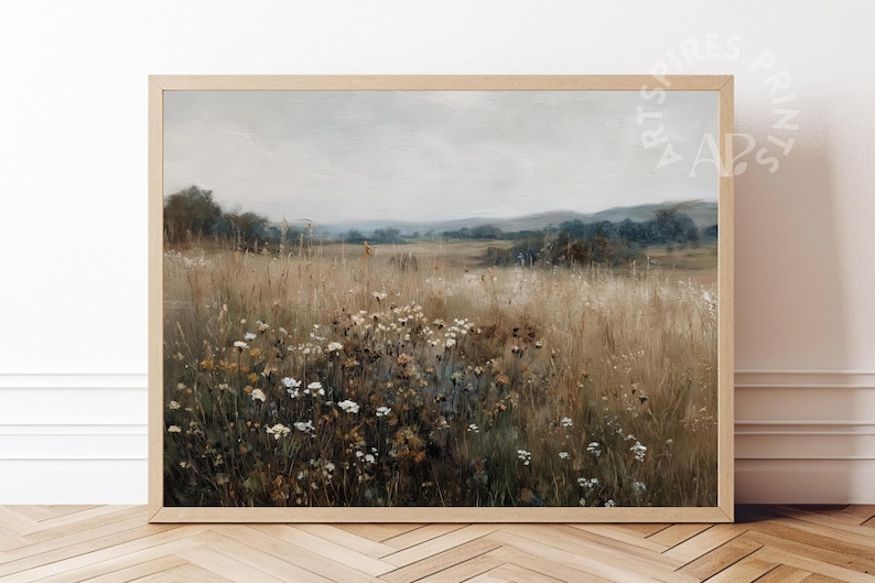 May include: A framed landscape print depicting a field of tall, dry grass and wildflowers beneath a cloudy sky. The artwork uses a muted palette of browns, greens, and whites, with a wooden frame.