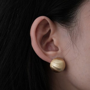 May include: A close-up of a person's ear with a gold-coloured, textured, round earring.
