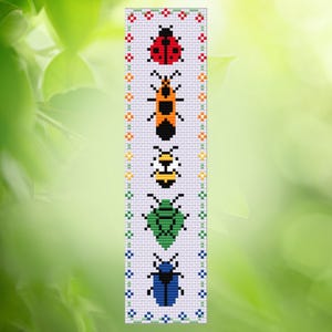 May include: A white bookmark featuring cross-stitch designs of various insects, including a red ladybug, an orange insect, a yellow bee, a green beetle, and a blue beetle. The edges are decorated with small floral patterns.