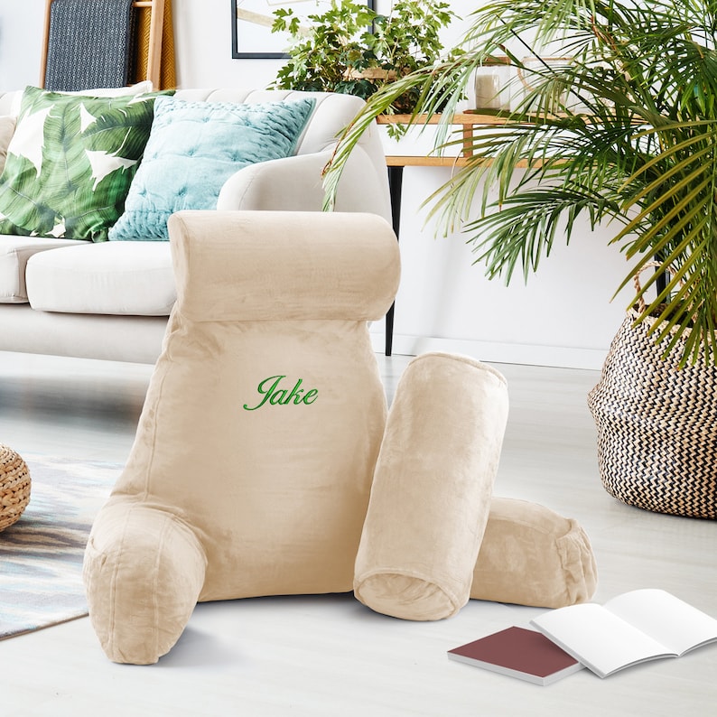 May include: A beige reading pillow with a matching lumbar pillow. The reading pillow has the name "Jake" embroidered on it in green.