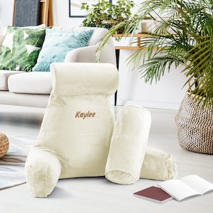May include: A large, cream-coloured reading pillow with a smaller pillow and a lumbar pillow. The reading pillow has the name "Kaylee" embroidered on it.