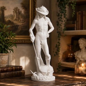 May include: A white matte sculpture of a standing figure wearing a wide-brimmed hat with a wreath detail. The figure holds a long, thin staff in one hand and rests a foot on a shield-like object. The base is circular and textured with small stones.