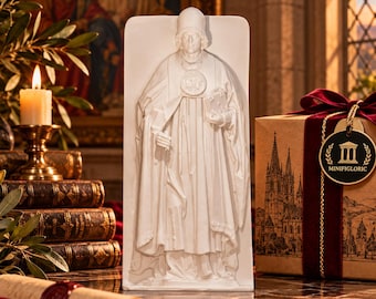 Könnte beinhalten: Eine weiße rechteckige Platte mit einem Relief eines in religiöse Gewänder gekleideten Menschen, der eine hohe Kopfbedeckung trägt und ein Buch hält. Die Platte steht neben einer Geschenkbox mit dunkelrotem Band und einem Etikett mit der Aufschrift MINIFIGLORIC.
