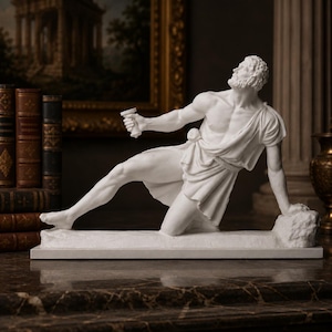 Può includere: Una scultura bianca opaca di una figura barbuta in posizione inginocchiata, che indossa un indumento drappeggiato. La figura guarda verso l'alto con un braccio teso che regge un piccolo oggetto cilindrico, mentre l'altra mano poggia su una base.