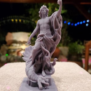 Może przedstawiać: Lawendowa statua męskiej postaci z płynącą draperią, stojąca na morskim stworze. Statua jest szczegółowa, z uniesionym ramieniem. Rzeźba stoi na prostokątnej podstawie.