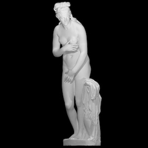Puede incluir: Estatua de mármol blanco de una mujer desnuda, parcialmente cubierta, de pie sobre un pedestal. La figura está en una pose clásica, con un brazo cubriendo su pecho y el otro a su lado. El fondo es negro.