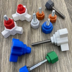 May include: Assortment of colourful plastic knobs with metal screws. The knobs are in various shapes, including round, square, and star-shaped. Some knobs are white, some are blue, some are red, and some are green.