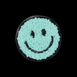 Op de afbeelding: Een ronde patch met een licht mintgroen, getextureerd en pluizig oppervlak met een geborduurd zwart smileygezicht. Het ronde embleem heeft een donkere rand en toont twee zwarte ogen en een gebogen zwarte mond.
