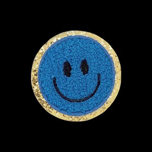 Puede incluir: Un parche circular que presenta una cara sonriente azul texturizada con ojos y una boca curva bordados en negro. El parche está enmarcado por un borde de material brillante de color dorado, creando un contraste con el centro azul.