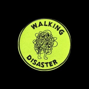 May include: A circular neon yellow embroidered patch with a black stitched border. The center features a black line-art graphic of a tangled scribble with two small legs. The text "WALKING DISASTER" is embroidered in black capital letters.