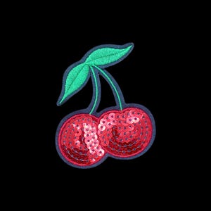Può includere: Una toppa ricamata a forma di ciliegie con due frutti rotondi ricoperti di paillettes rosse lucide. La toppa presenta una foglia e dei gambi ricamati in verde brillante, il tutto delineato da un bordo blu scuro su sfondo nero.