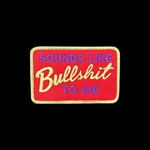 Peut inclure: Un écusson rectangulaire brodé avec un fond rouge et une bordure dorée. Le texte "SOUNDS LIKE" et "TO ME" est brodé en violet, tandis que le mot "Bullshit" est brodé dans une grande police cursive dorée au centre de l'écusson.