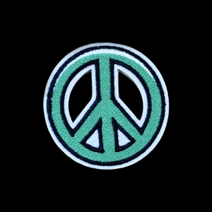 Puede incluir: Un parche bordado circular que presenta un símbolo de la paz en color verde menta. El diseño está delineado con un borde negro grueso y un borde exterior blanco fino, creando un elemento gráfico de alto contraste para diversas telas.