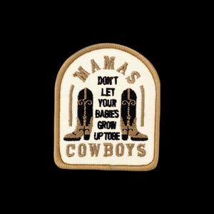 May include: An embroidered patch with a cream-colored background and a tan border. It features two black and tan cowboy boots flanking the text 'MAMAS DON'T LET YOUR BABIES GROW UP TO BE COWBOYS' in black and tan lettering, arranged in a rounded shape.