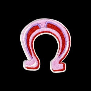 Könnte beinhalten: Ein gestickter Aufnäher in Hufeisenform mit konzentrischen Bändern aus hellrosa, leuchtend rotem und zart lavendelfarbenem Garn. Das Design hat eine dicke, erhabene Textur mit einem weißen Rand, der eine deutliche Hufeisensilhouette bildet.